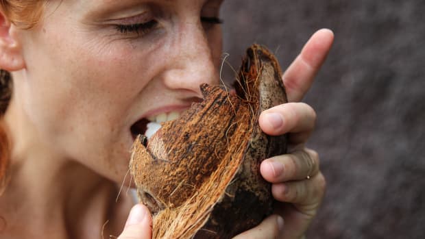 woman bites into a coconut.