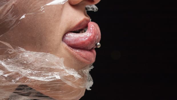 a person wrapped in plastic with a pierced tongue sticking out of their mouth
