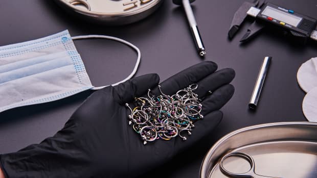 piercing equipment and a person's hand filled with piercing jewelry.