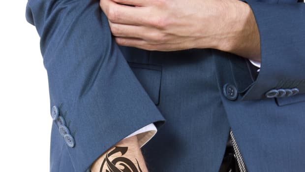 Man in a suit showing his arm tattoo.