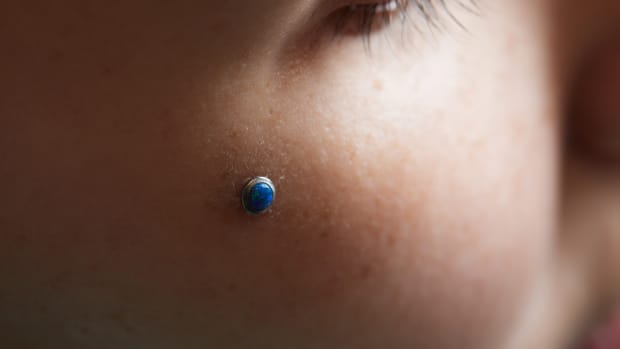person with a blue dermal piercing in their cheek.