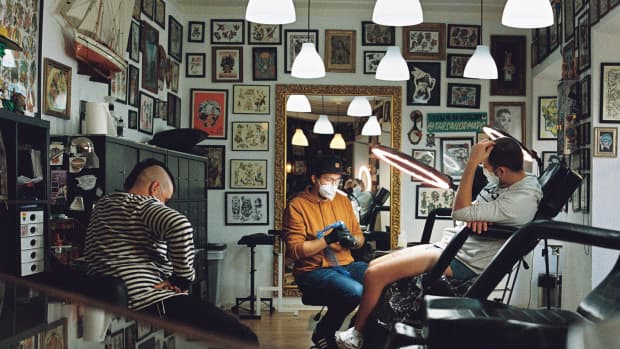 tattoo artist, client, and another person sit in tattoo shop.